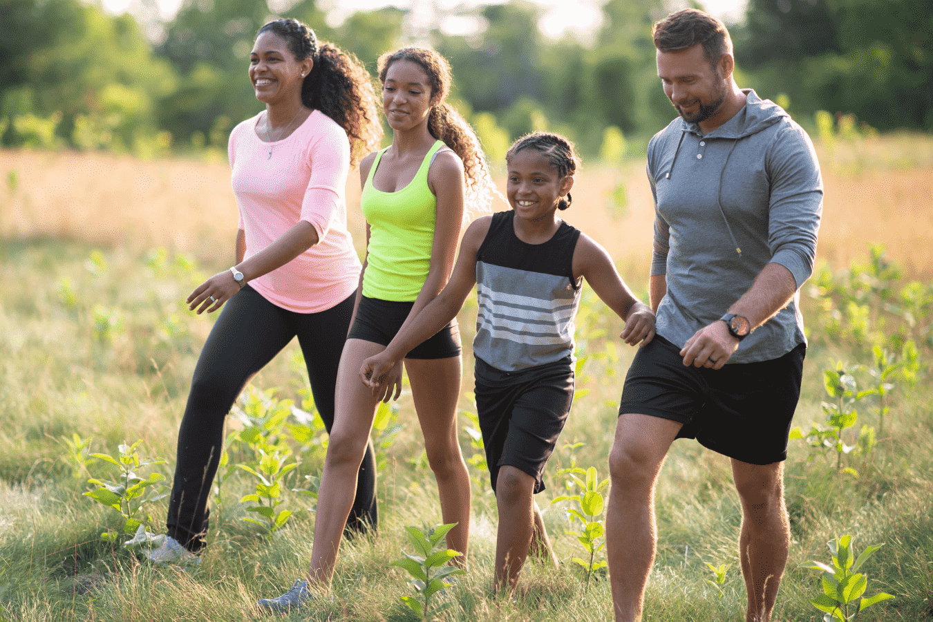 A mixed-racial couple and their two children, a young boy and an older girl, walk through a field while doing a family exercise