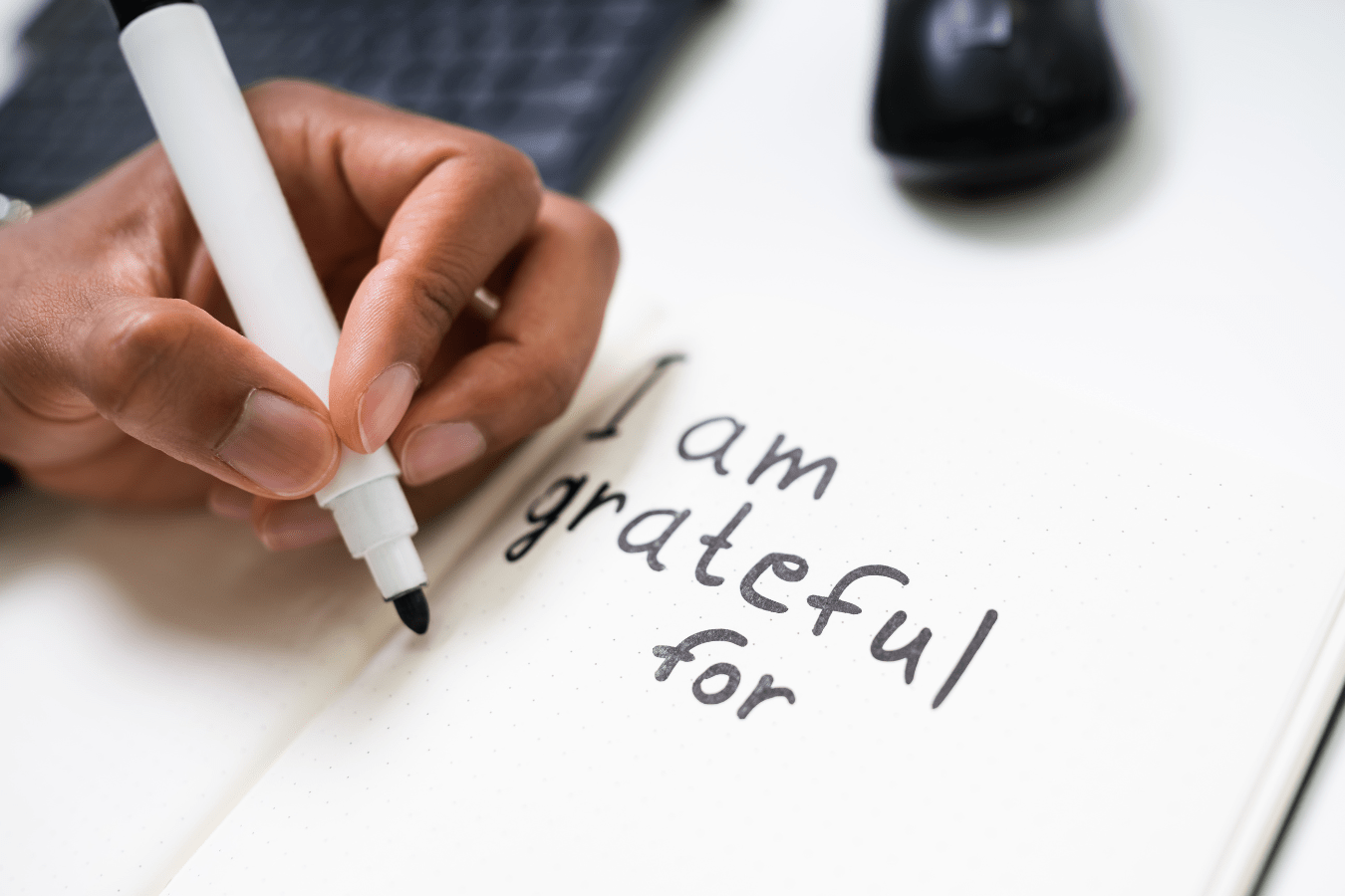 A child's hand writing "I am grateful for" in black marker in a gratitude journal